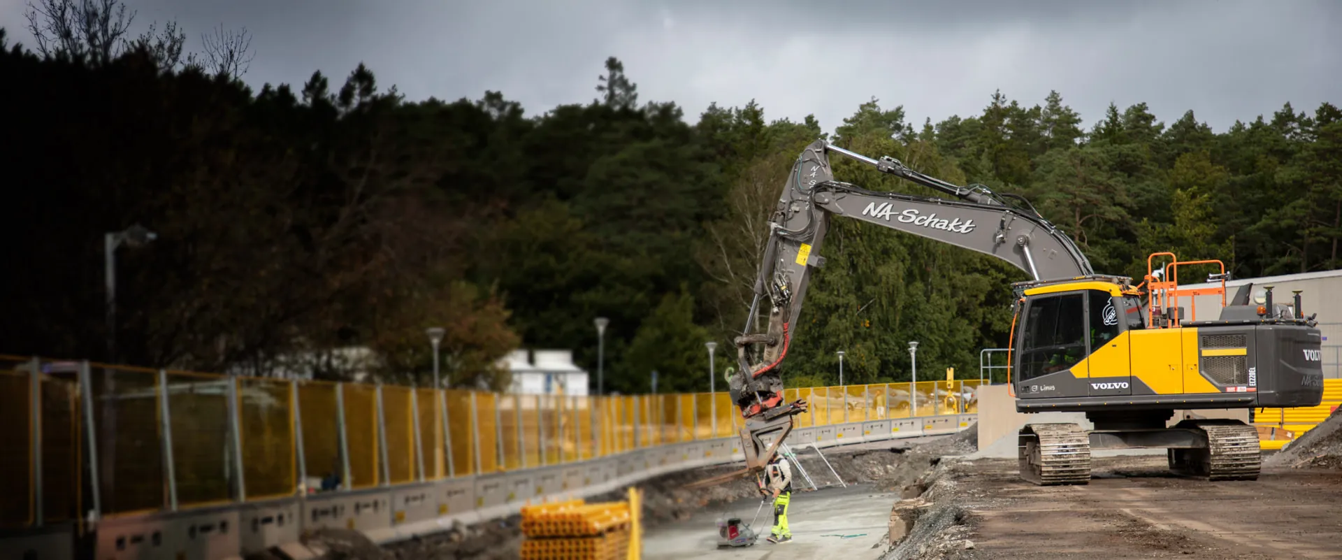Gul NA Schakt-grävmaskin på byggarbetsplats med gula skyddsstängsel